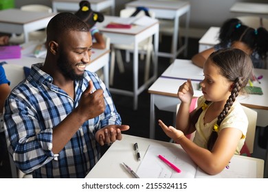 African american young male teacher teaching sign language to caucasian elementary girl in class. unaltered, education, childhood, learning, teaching, disability and school concept. - Powered by Shutterstock