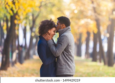 African american young man kissing his girlfriend forehead while walking in autumn city park, copy space