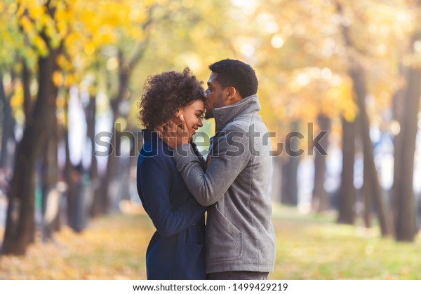 African american young man\
kissing his girlfriend forehead while walking in autumn city park,\
copy space