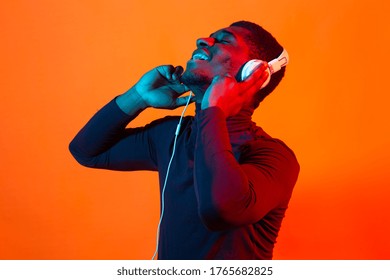 African american young man listening to music online dancing and singing with headphones, neon light. Music and technology concept.