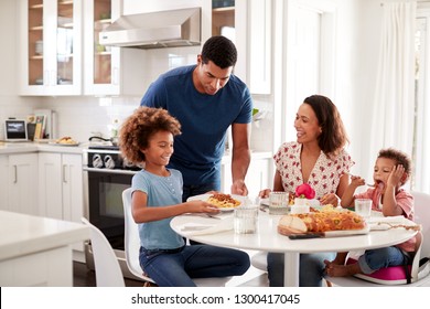 African American young mother sitting at table in the kitchen with children, father serving them food, selective focus