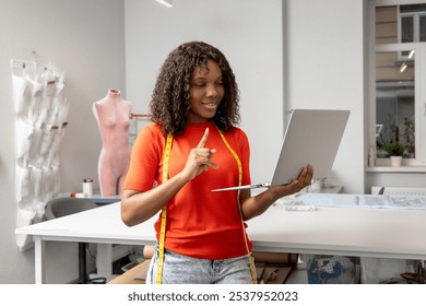 African american young seamstress with a laptop discussing something on the phone - Powered by Shutterstock