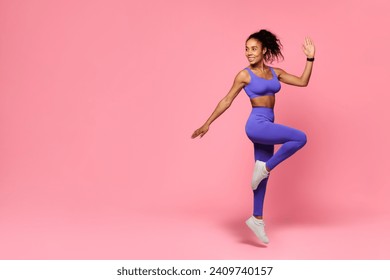 African American young sporty woman in activewear jumps performing cardio workout, looking aside at free space for gym offer, over pink studio background, advertising healthy sport - Powered by Shutterstock