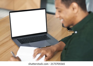 African American young student or freelancer man working remotely, takes notes, communicates online using video call sitting at workplace with laptop with blank screen, mockup