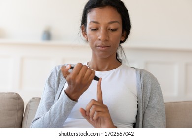 African American Young Woman Sit On Couch And Use Glucometer, Measure Glucose Or Blood Sugar Test At Home, Take Blood For Analysis From Finger, Diabetes, Healthcare And Medical Concept