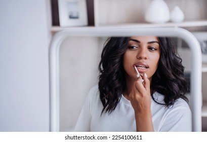 African American young woman with wavy hair doing make up at mirror. Attractive brunette Brazilian female model preparing for shoot. Cosmetics, women routine. Pretty tanned girl preening for date. - Powered by Shutterstock