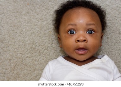 African American/Black boy, six months old laying down looking surprised with his eyes open wide