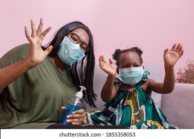 African Americans' Mother And Daughter Wearing A Mask Are Washing Their Hands With Alcohol To Protect Them From Germs And COVIC 19 While Staying At Home. Black People Or African Americans