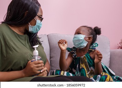 African Americans' Mother And Daughter Wearing A Mask Are Washing Their Hands With Alcohol To Protect Them From Germs And COVIC 19 While Staying At Home. Black People Or African Americans