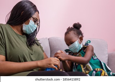 African Americans' Mother And Daughter Wearing A Mask Are Washing Their Hands With Alcohol To Protect Them From Germs And COVIC 19 While Staying At Home. Black People Or African Americans