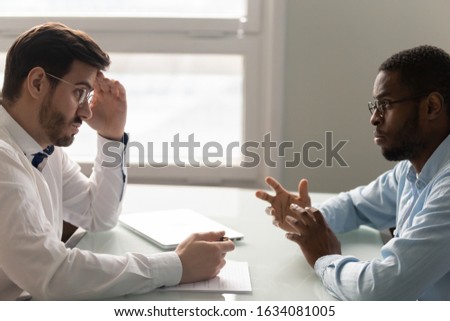 African applicant Caucasian HR manager sitting in front of each other during job interview, owner listens vacancy candidate with mistrust, bad first impression, negative attitude racial discrimination