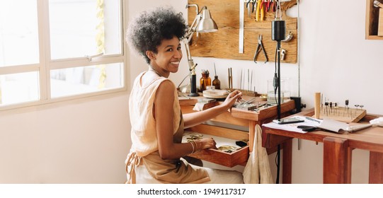 African artist glancing back while working at jewelry workshop. Cheerful young female worker in a jewelry workshop. - Powered by Shutterstock