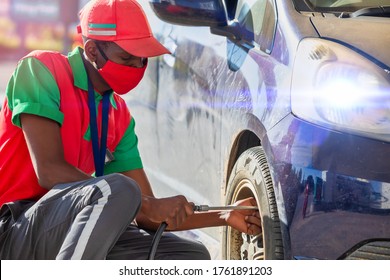 African Attendant At A Petrol Station Inflating The Tires Of A Small Budget Car