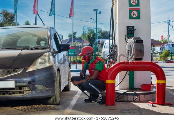 African attendant at a petrol station inflating the\
tires of a small budget\
car