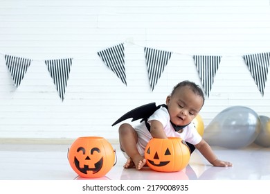 African baby child girl wearing black winged vampire with orange candy bucket Jack O lantern, Haloween costume, Happy Halloween
