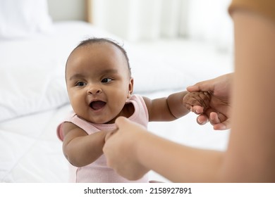 African Baby Girl Learning To Walk And Mother Or Sitter Holding Hands On Bedroom 