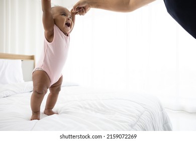 African Baby Girl Learning To Walk And Mother Or Sitter Holding Hands On Bedroom