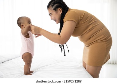 African Baby Girl Learning To Walk And Mother Or Sitter Holding Hands On Bedroom