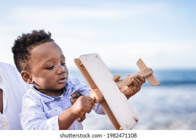 African baby having playful time with wood airplain on the beach - Family, father and toddler love