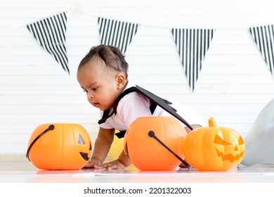 African Baby Kid Dressing Up In Vampire Fancy Halloween Costume With Black Bat Wings, Little Cute Child Go To Party, Play Trick Or Treat, Hold Orang Pumpkin Basket. Happy Halloween Celebration.