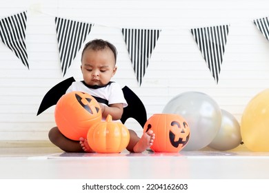 African Baby Kid Dressing Up In Vampire Fancy Halloween Costume With Black Bat Wings, Little Cute Child Go To Party, Playing Trick Or Treat, Holding Orang Pumpkin Basket. Happy Halloween Celebration.