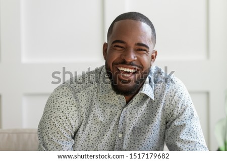 African bearded man having wide sincere toothy smile look at camera laughing, guy vlogger recording filming new vlog at home indoors share funny information with internet audience, head shot portrait
