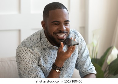 African bearded man sitting on couch holds smartphone speaks with girlfriend on speakerphone, convenient easy method of hands-free phone usage, make phone call through device external speakers concept - Powered by Shutterstock - Get 15% off with code: PIKWIZARD15