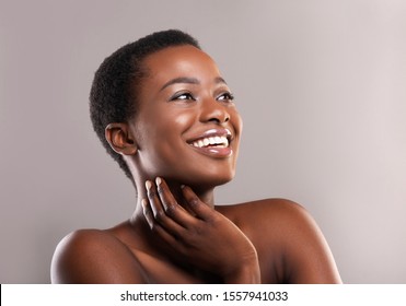 African Beauty. Portrait Of Happy Beautiful Black Woman Touching Her Soft Skin And Looking Upwards At Copy Space On Grey Background