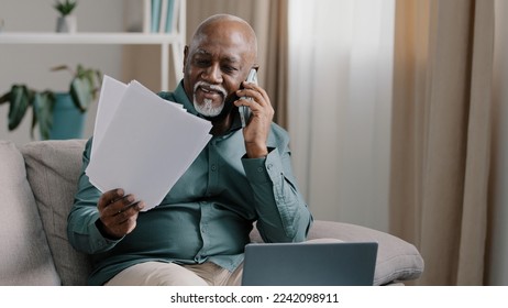 African biracial bald old man with gray beard senior mature businessman busy employee using laptop talking cell phone in multitasking discussing online project distant paper documents remote from home - Powered by Shutterstock