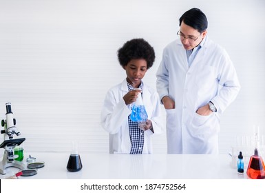 African black boy student and asian male professor in white gown is learning and test science chemical with colorful liquid in beaker in lab room at to school. Education and science research concept.