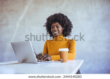 African black business woman working on laptop at office. Smiling mature african american businesswoman lookingup at copy space while working on phone. Successful woman entrepreneur 
