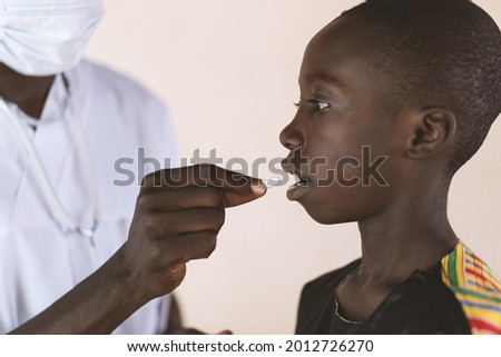 African black Doctor giving medical pill or vitamin supplement to a little native African child.