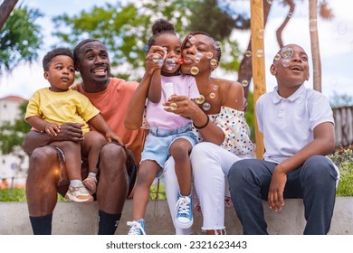 African black ethnic family with children in playground blowing soap bubbles next to park trees at sunset - Powered by Shutterstock