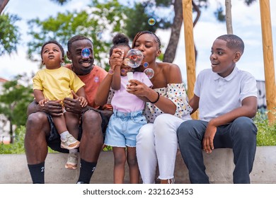 African black ethnicity family with children in playground having fun blowing soap bubbles next to trees in the park - Powered by Shutterstock