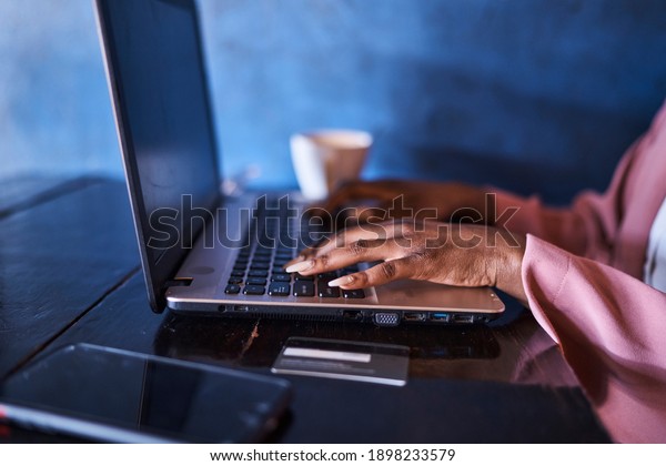 African Black female using credit card to\
make payment for online purchase while sitting in restaurant typing\
on a black and silver laptop with coffee and cell phone on table\
Randburg, Johannesburg