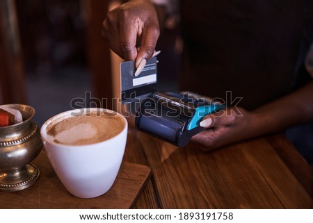 African Black female waitress swiping a credit card through a mobile card machine for cappuccino in restaurant Randburg, Johannesburg, Gauteng South Africa