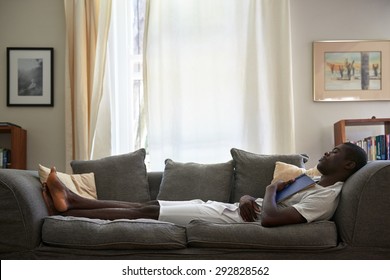 african black man sleeping on sofa couch while reading book at home living room lounge