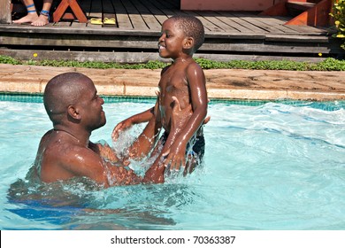 African Black Man And Son Swimming In Bright Sunlight In Pool