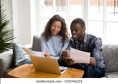 African black positive married couple sitting on sofa at home read documents paper checking bills, bank account balance feeling satisfied and happy. Refund income last loan payment good news concept