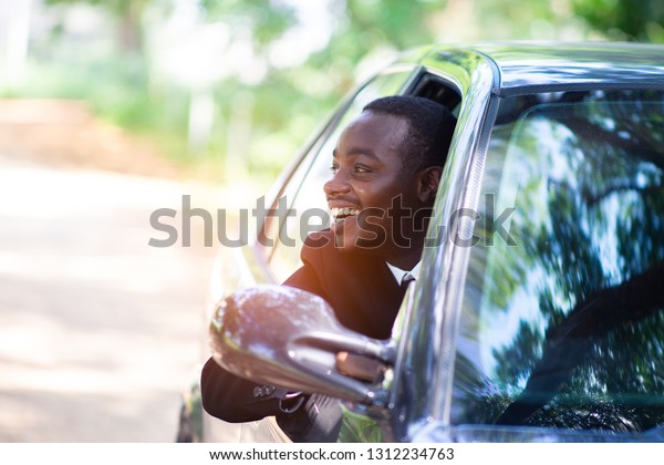 African business man driving and  smiling\
while sitting in a car with open front\
window.