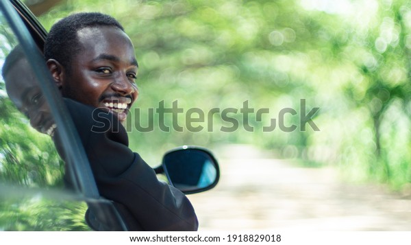 African business man driving and \
smiling while sitting in a car with open front window.16:9\
style