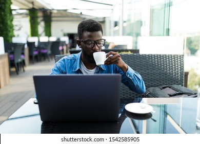 African business man sitting at table in cafe working with laptop and papers and drinking coffee