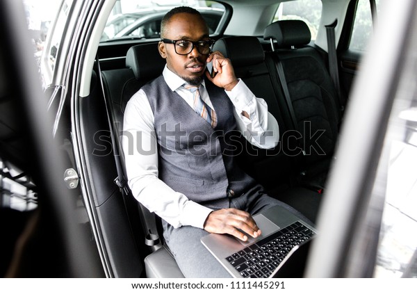 African businessman in the back seat of a car\
talking on the phone