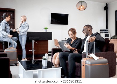 African businessman discussing ideas with female colleague while sitting on sofa in airport business lounge, busy businesspeople working on tablet during waiting flight at airport departure lounge - Shutterstock ID 2366301311