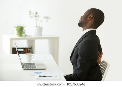 African Businessman Feels Strong Backache Sitting On Uncomfortable Office Chair At Work, Black Man In Suit Suffering From Ache Pain In Tensed Back Muscles After Sedentary Work In Incorrect Posture