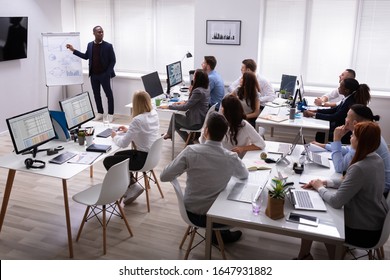 African Businessman Giving Presentation To His Colleagues Sitting On Table With Computers In Office