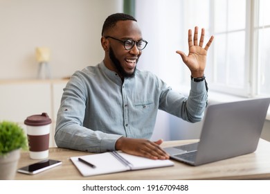 African Businessman Making Video Call Online Via Laptop Computer Waving Hello To Webcam Sitting At Workplace In Modern Office. Remote Business Communication Concept