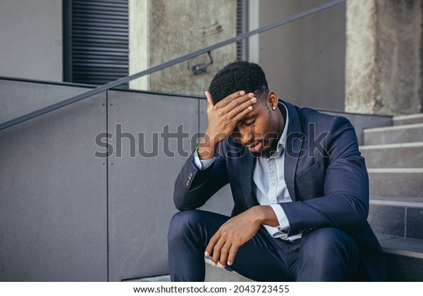 african businessman sitting frustrated on the stairs\
depressed by the results of his work, holding hands behind his\
head