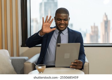 African businessman in waving during virtual meeting professional video call interaction, online communication with tablet remote work concept, corporate setting, modern office with cityscape view - Powered by Shutterstock