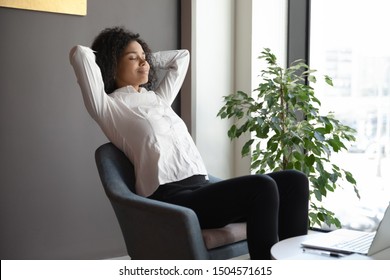 African businesswoman relaxing on armchair in office lobby relaxing with closed eyes feels serenity, no stress, anxiety and stress reducing after workday, daydreaming about successful career concept